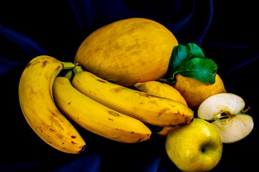 yellow fruit on a black background with melon bananas apples and lemons