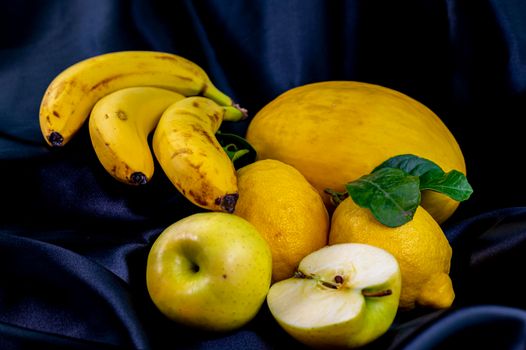 yellow fruit on a black background with melon bananas apples and lemons