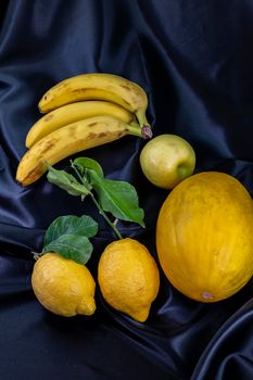 yellow fruit on a black background with melon bananas apples and lemons