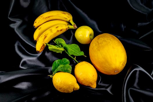 yellow fruit on a black background with melon bananas apples and lemons