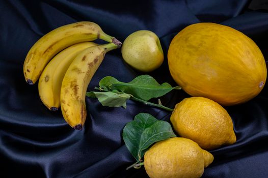 yellow fruit on a black background with melon bananas apples and lemons