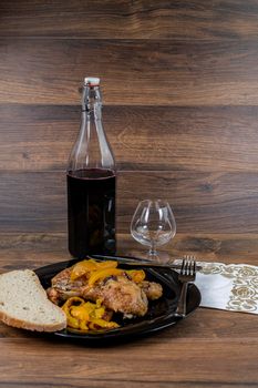 chicken legs and yellow peppers with glass bread and cutlery on black plate wood background