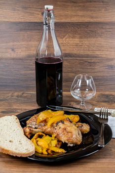 chicken legs and yellow peppers with glass bread and cutlery on black plate wood background