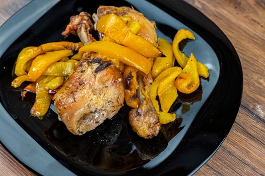 chicken legs and yellow peppers with glass bread and cutlery on black plate wood background