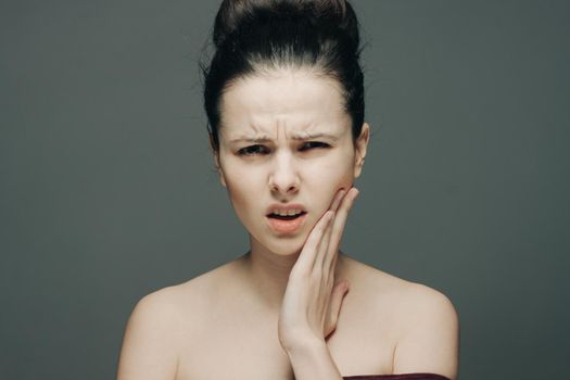 brunette displeased expression holding hand on face gray background. High quality photo