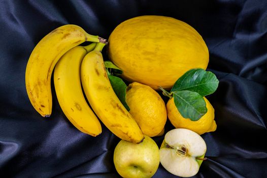 yellow fruit on a black background with melon bananas apples and lemons