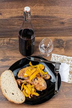 chicken legs and yellow peppers with glass bread and cutlery on black plate wood background