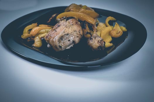 chicken so with yellow peppers on a black plate white background