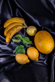 yellow fruit on a black background with melon bananas apples and lemons