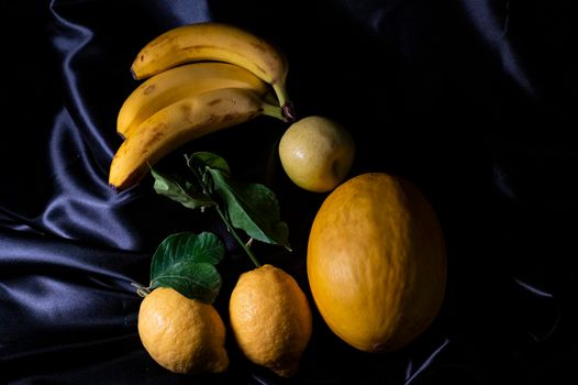 yellow fruit on a black background with melon bananas apples and lemons