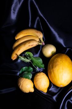 yellow fruit on a black background with melon bananas apples and lemons