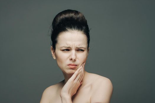 brunette displeased expression holding hand on face gray background. High quality photo