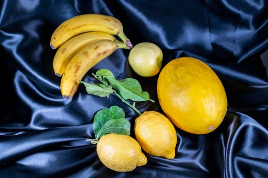yellow fruit on a black background with melon bananas apples and lemons