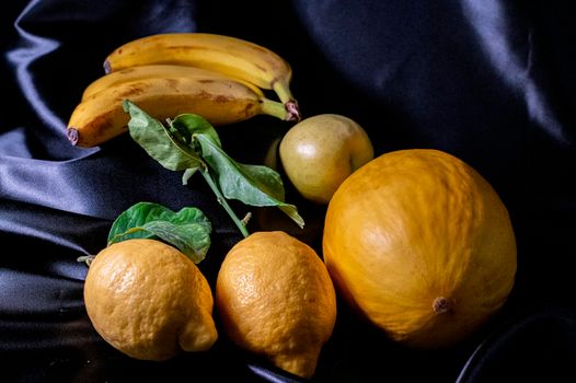 yellow fruit on a black background with melon bananas apples and lemons