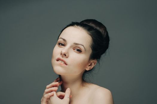 nude woman with hairstyles in her head touches her face with her hands on a gray background. High quality photo