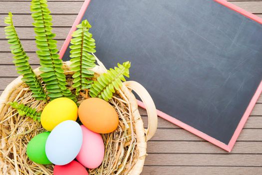 Colorful easter eggs in the basket and blackboard on wood background with space