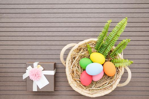 Colorful easter eggs in the basket and gift box on wood background with space