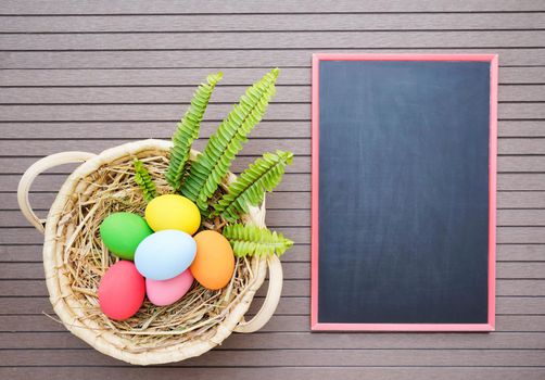 Colorful easter eggs in the basket and blackboard on wood background with space