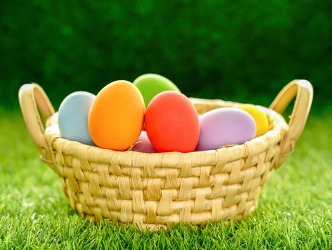 Colorful easter eggs in the basket on green grass background with copy space