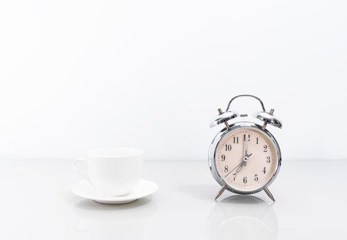 Silver alarm clock and coffee cup on table