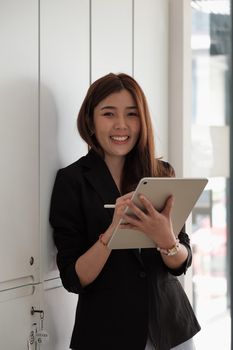 Portrait of Asian Businesswoman smiling in black suit holding aa tablet.