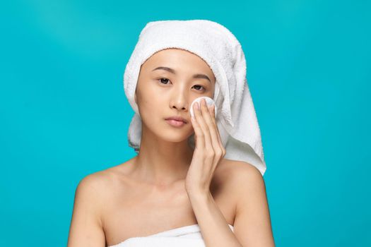 woman of asian appearance naked shoulders clear skin cotton pad blue background. High quality photo