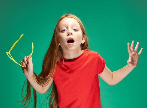 red-haired girl holding glasses in her hands red t-shirt emotions green background. High quality photo