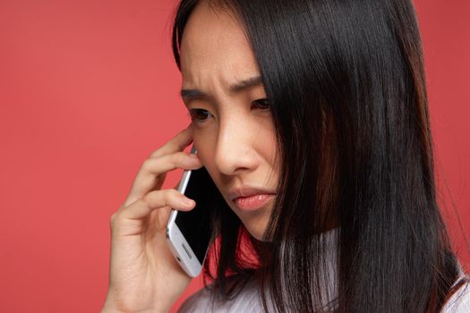 woman of asian appearance and contented facial expression talking on the phone close-up red fund. High quality photo