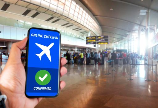 The hand of a man holding a mobile phone with the online check in confirmation message on the screen inside an airport. Travel and technology concept. Online ticket booking.