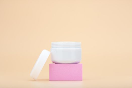 White opened cosmetic jar on pink podium against beige background with copy space. Concept of beauty products for skin care, body care or hair care. Face cream, scrub or mask enriched with natural oil