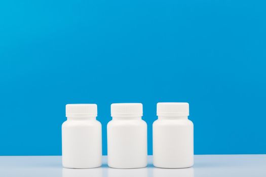 Three white medication bottles on white table against blue background with copy space. Concept of vitamins, supplements, medication and healthcare. High quality photo
