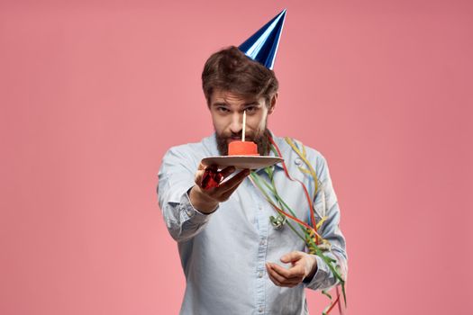 Man with cake in a plate and in a blue shirt on a pink background birthday holidays cropped view. High quality photo