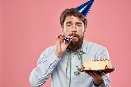 Man with cake in a plate and in a blue shirt on a pink background birthday holidays cropped view. High quality photo