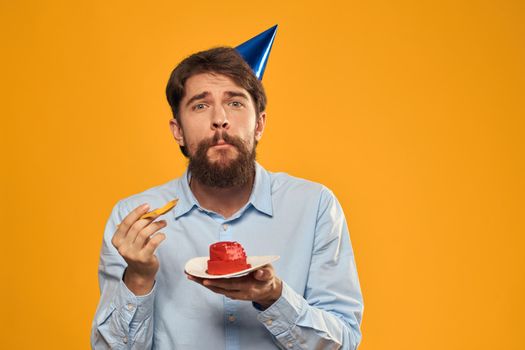 a man with a birthday cake in his hands and in a cap on a yellow background on his birthday. High quality photo