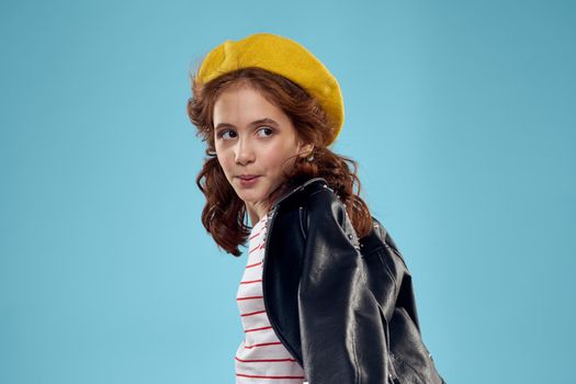 Fashionable girl in a black leather jacket on a blue background and a yellow hat on her head. High quality photo