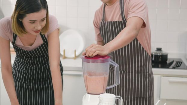 Happy young family couple husband and wife making fresh apple smoothie in kitchen together. The man and woman help each blender the apples with a juice blender. Healthy lifestyle concept,