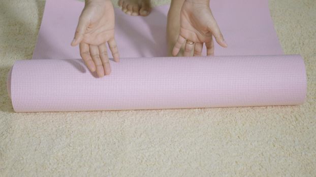 Asian young woman rolling fitness yoga pink mat before sports practice for exercise, female working out at home in the living room. lifestyle sport healthy concept, slow motion from 60fps