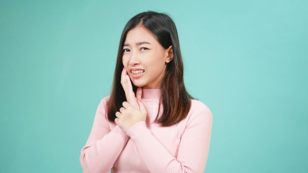 Portrait young Asian beautiful woman wear silicone orthodontic retainers on teeth feeling pain toothache holding her cheek with hand isolated on blue background. Female suffering teeth pain dental