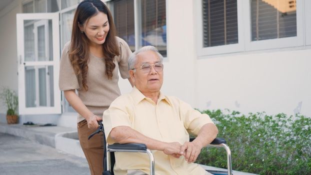 Disabled senior man on wheelchair with daughter, Happy Asian generation family having fun together outdoors backyard, Care helper young woman walking an elderly man smiling and laughed