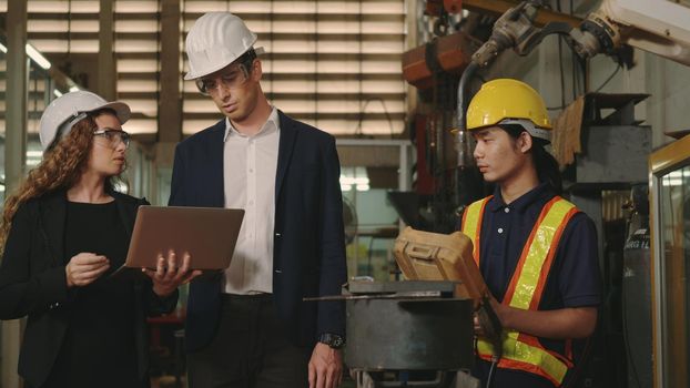 Three heavy industry business engineering in hardhats discuss information on laptop computer while standing indoors welding manufacturing industrial for check and control automated programming