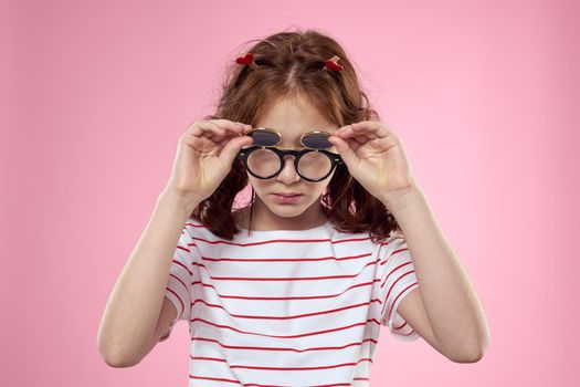 little girl in fashionable glasses and clothespins on her hair emotions pink background hearts. High quality photo