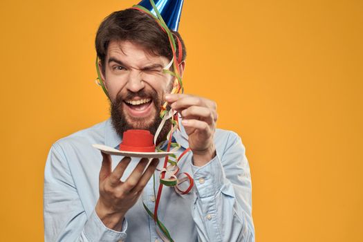 Cheerful man with a cake on a yellow background birthday holidays cap on his head. High quality photo