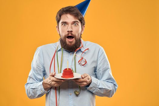 Cheerful man with a cake on a yellow background birthday holidays cap on his head. High quality photo