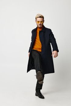 modern man in a dark coat and full-length trousers on a light background and glasses on his face. High quality photo