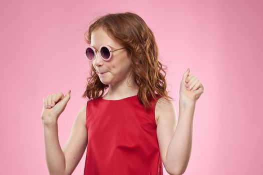Girl with curly hair dark round glasses fun red dress pink background. High quality photo