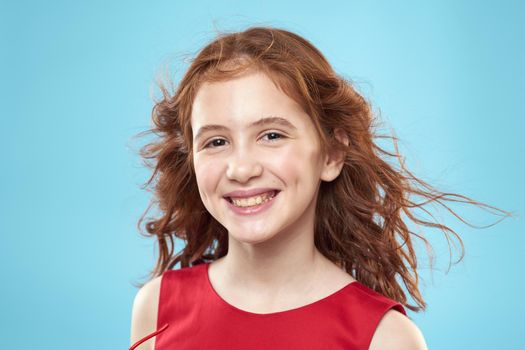 little girl with curly hair with a crown on her head red dress Smile blue background. High quality photo