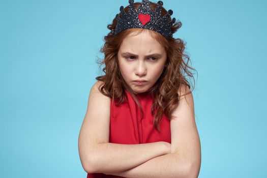 Girl with curly hair with a crown on her head red dress lifestyle blue background. High quality photo