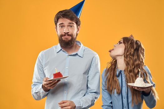 Birthday party man and woman in a cap with a cake on a yellow background cropped view. High quality photo