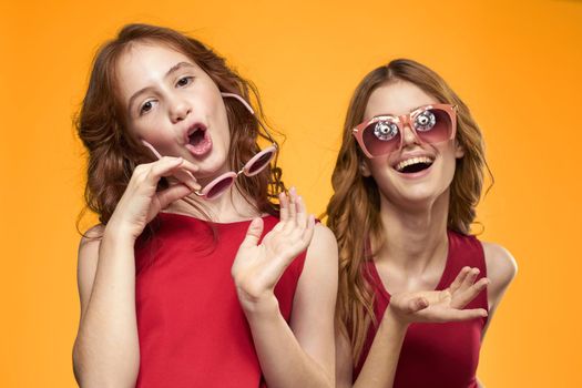 cheerful mom and daughter wearing sunglasses lifestyle friendship family yellow background studio. High quality photo