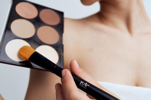Pretty woman with naked shoulders applying makeup on face lifestyle. High quality photo